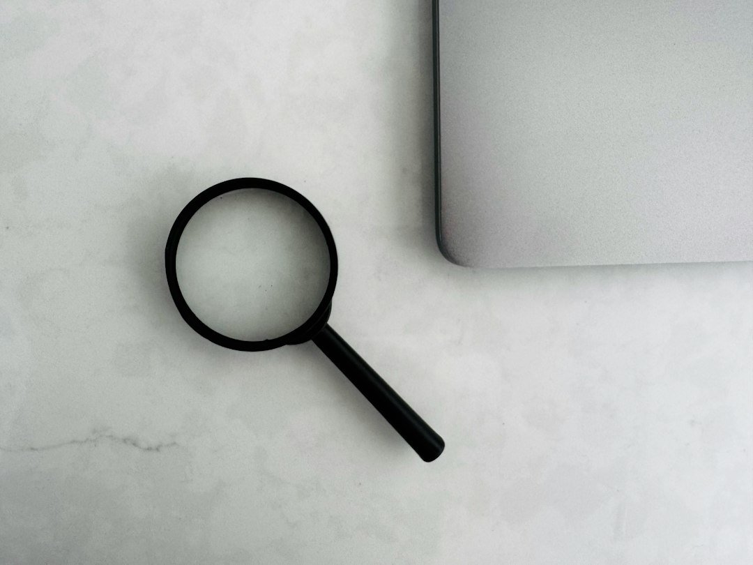 Magnifying glass next to a laptop on a marble surface